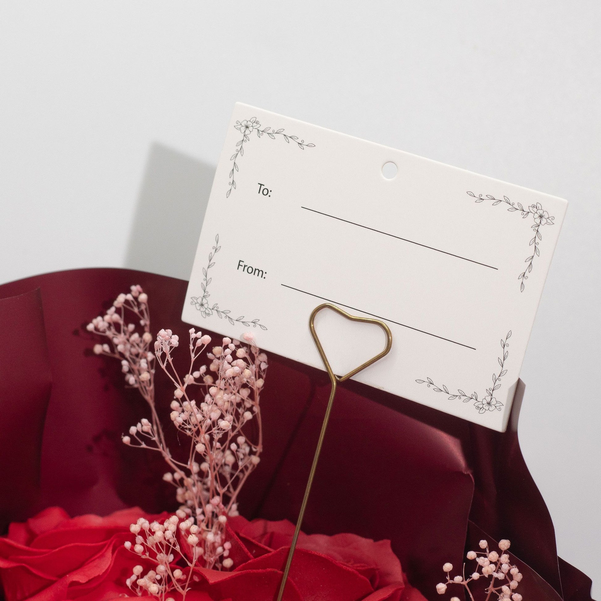 Etiqueta para ramo de rosas rojas, con soporte dorado en forma de corazón y fondo floral. Ideal para regalar.