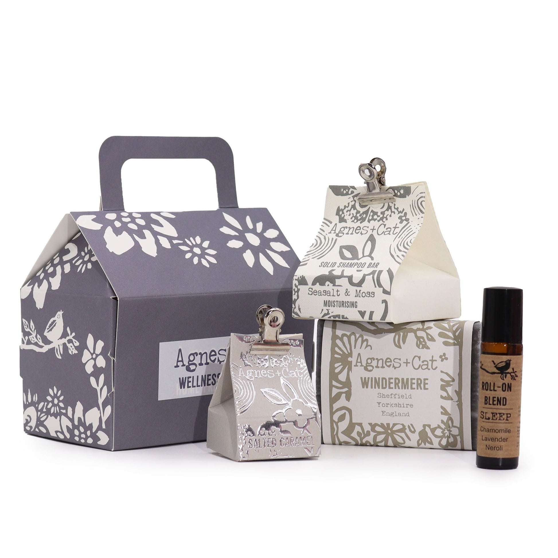 Conjunto de bienestar Agnes & Cat: caja gris, champú sólido, jabón Windermere y roll-on de aromaterapia sobre fondo blanco.