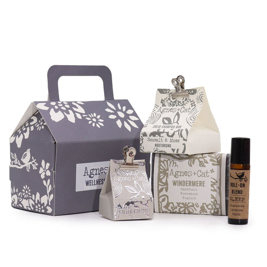 Conjunto de bienestar Agnes & Cat: caja gris, champú sólido, jabón Windermere y roll-on de aromaterapia sobre fondo blanco.