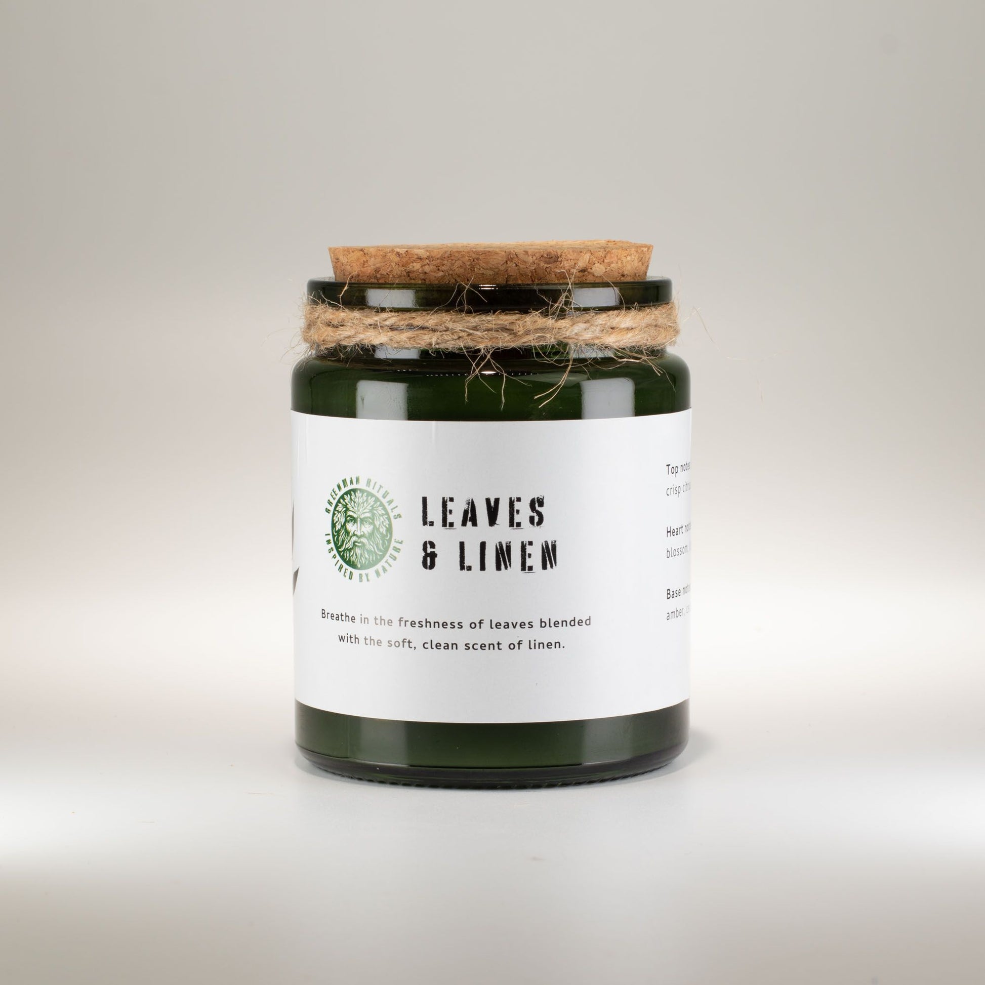 Vela aromática verde en frasco de vidrio con tapa de madera, fragancia a hojas y lino.