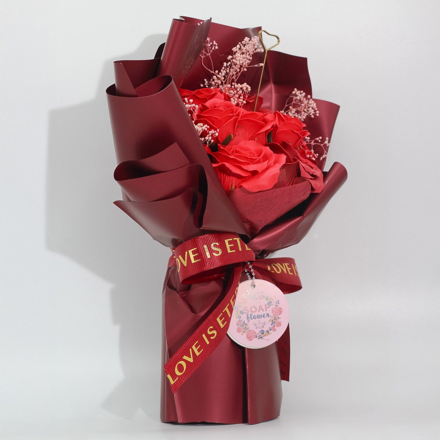 Ramo de flores rojas con envoltura burdeos y cinta "LOVE IS ETERNAL" para regalo romántico y elegante.