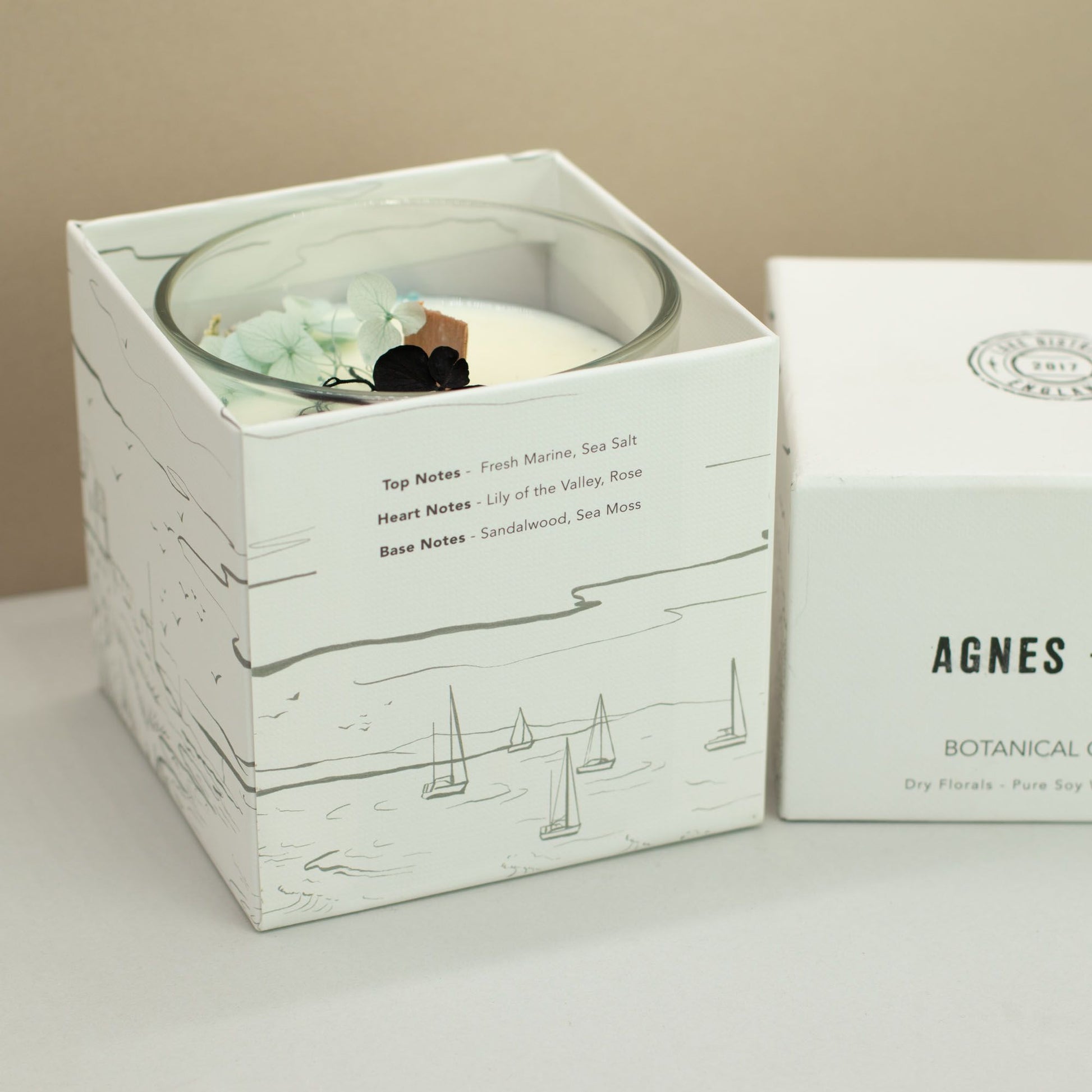 Vela de soja en recipiente transparente, aroma floral con notas de mar y rosa, presentada en caja blanca decorativa.
