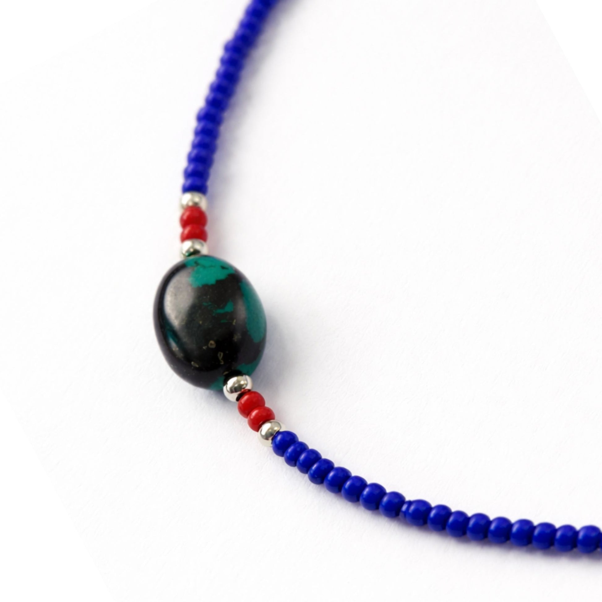 Collar de cuentas azules con detalles en rojo y una piedra ovalada negra y verde, estilo bohemio.