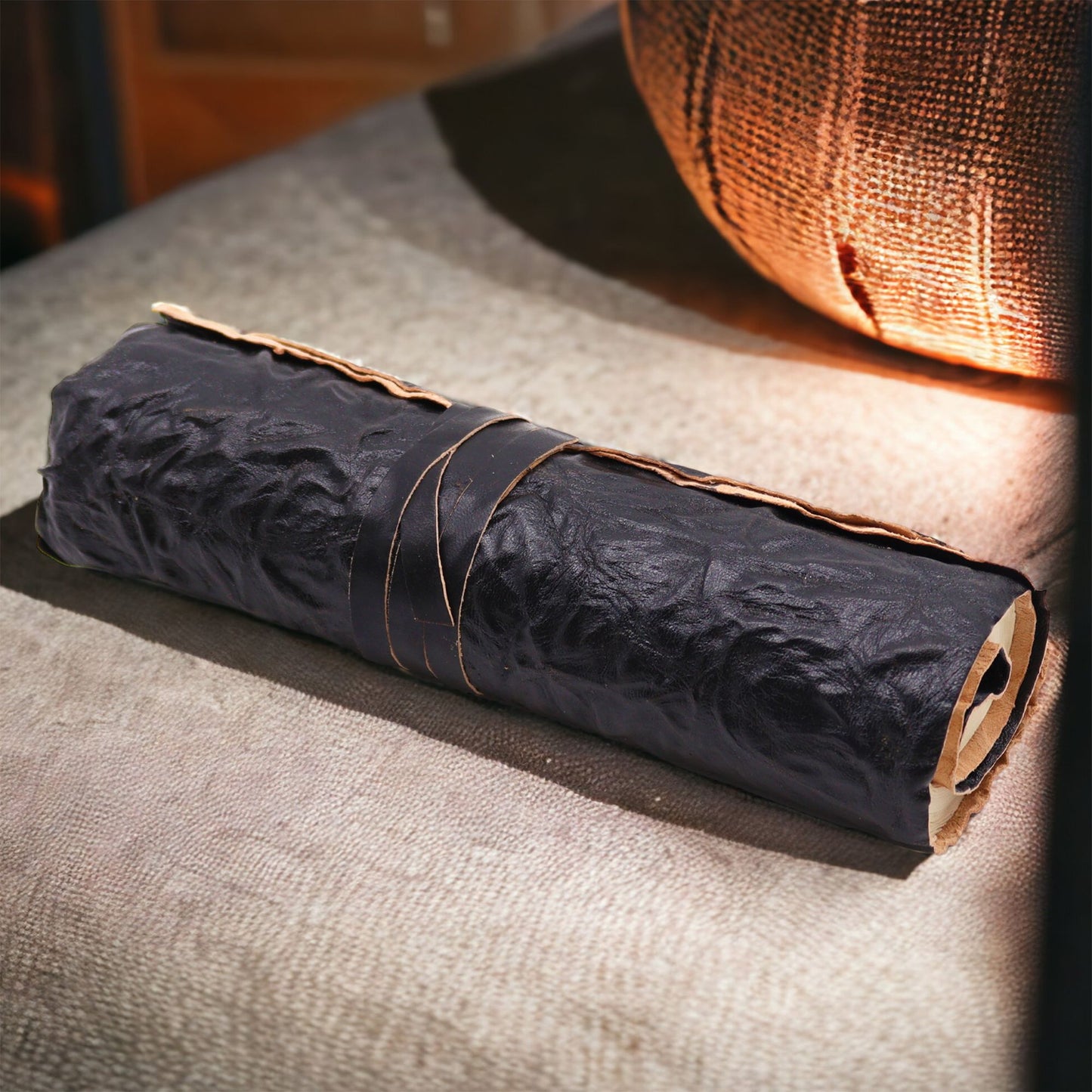 Papel kraft negro enrollado con cinta de cuero, textura arrugada, ideal para manualidades y regalos.