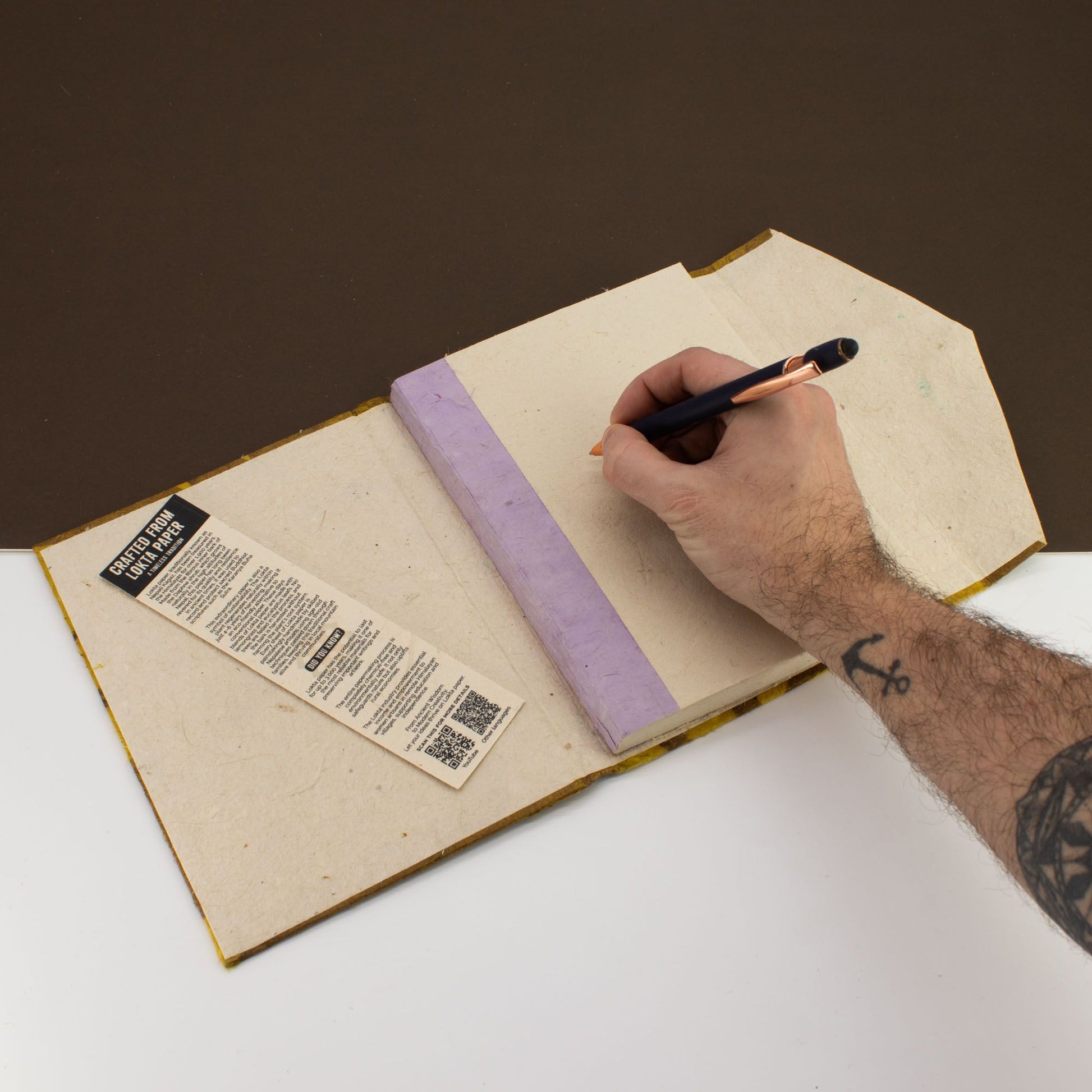 Cuaderno ecológico de papel reciclado, tapa color lavanda, con pluma negra, estilo minimalista.