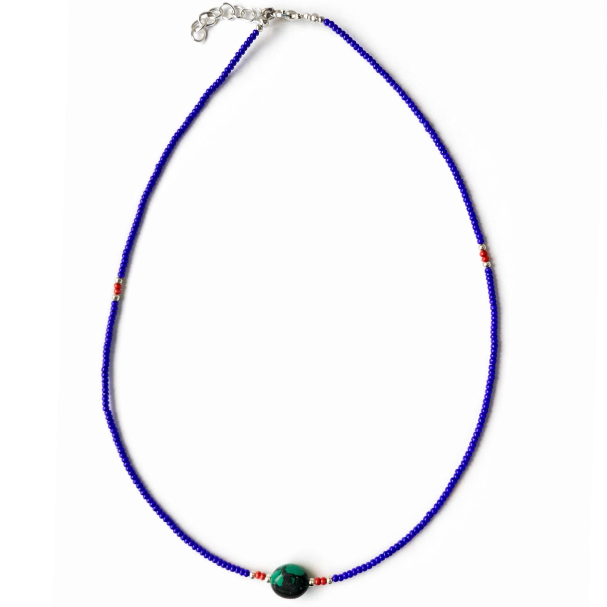 Collar de cuentas azules, con detalles en rojo y una piedra verde, estilo bohemio.