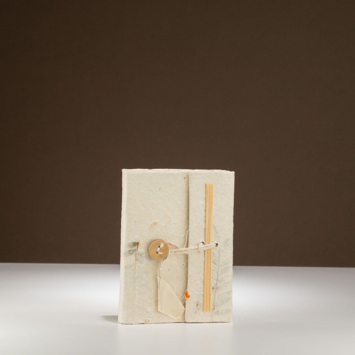 Cuaderno artesanal de papel reciclado en color blanco, cerrado con un botón de madera y atado con cuerda natural.