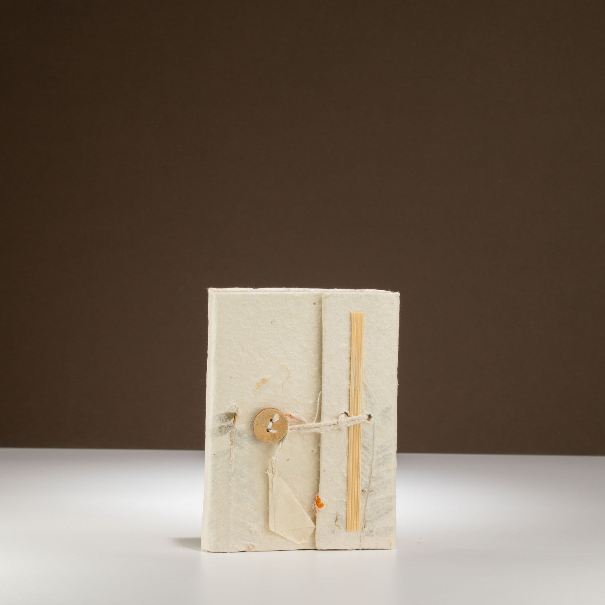 Cuaderno artesanal de papel reciclado en color blanco, cerrado con un botón de madera y atado con cuerda natural.