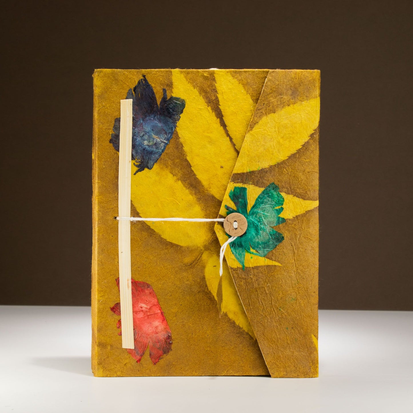 Cuaderno artesanal amarillo con flores azules y rojas, atado con cuerda, estilo bohemio y material ecológico.