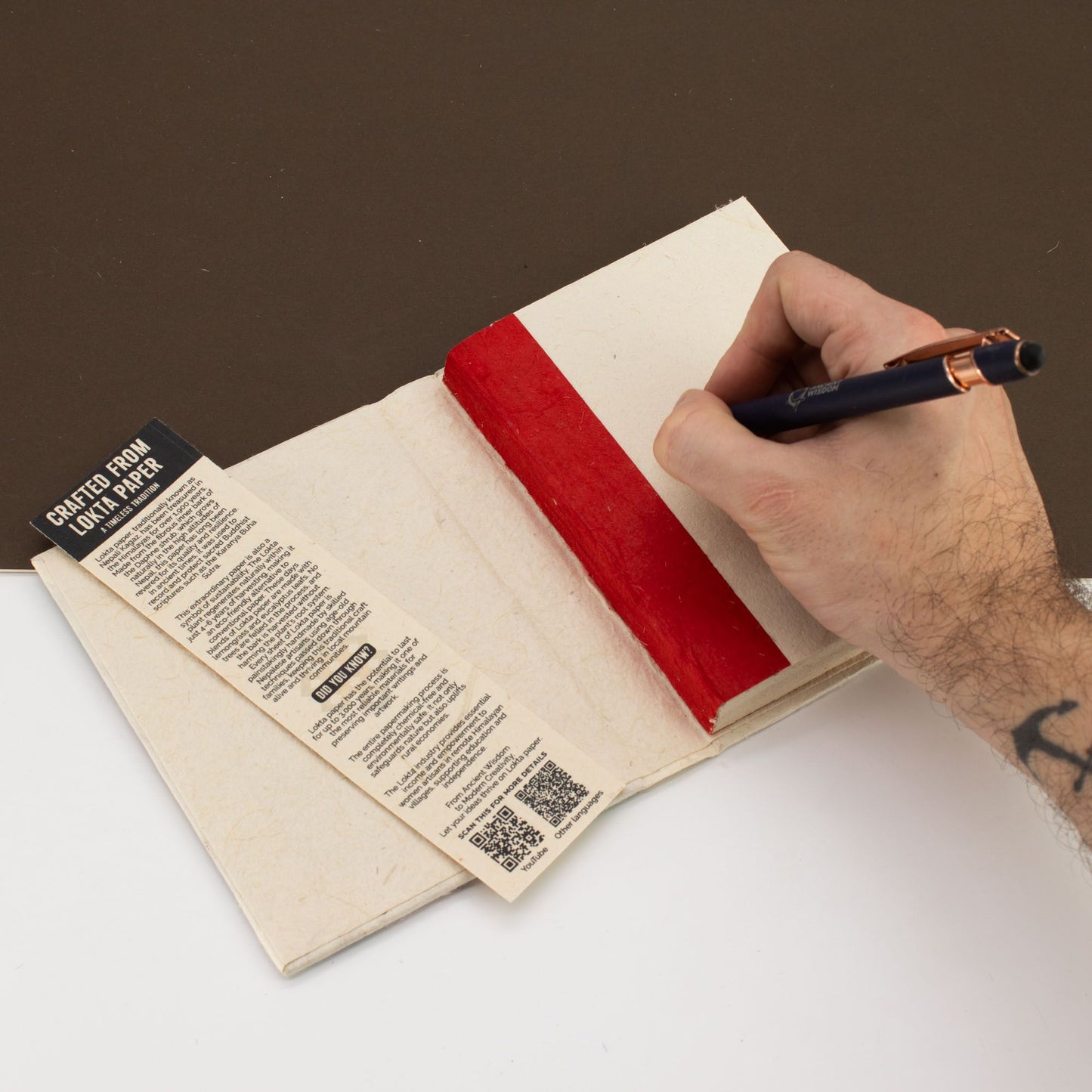 Cuaderno artesanal de papel reciclado con borde rojo y etiqueta negra, perfecto para escribir y tomar notas.