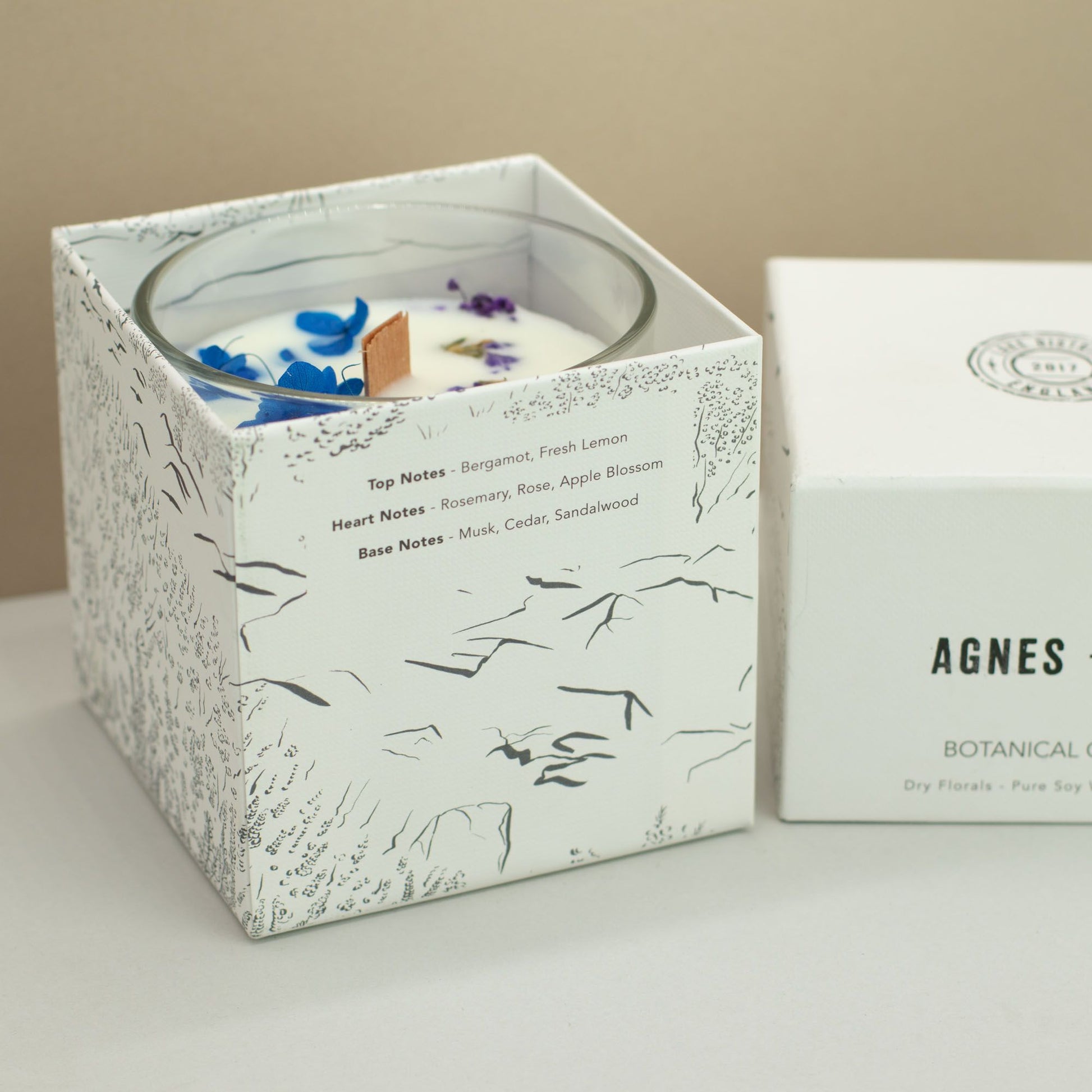 Vela de soya blanca con notas de bergamota y rosa, en caja decorativa con dibujos botánicos en negro.