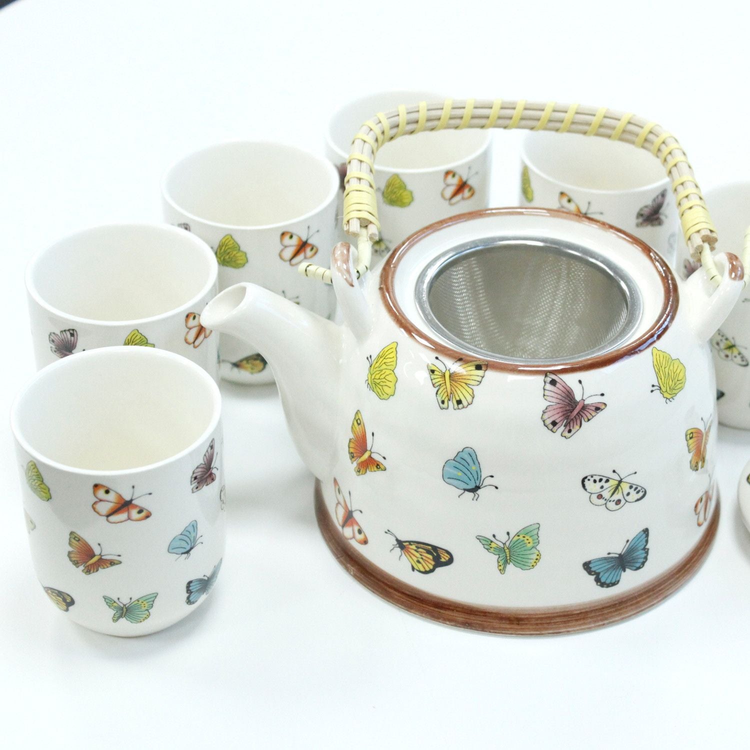 Tetera blanca con mariposas coloridas y filtro, incluye seis tazas a juego, estilo elegante y moderno.