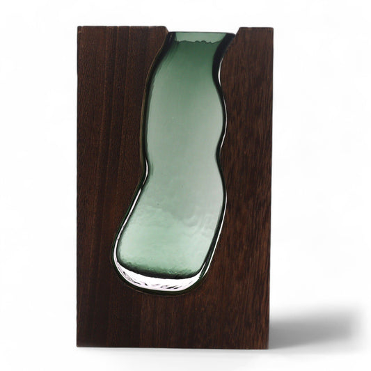 Jarrón de cristal verde con forma orgánica encajado en un bloque de madera rectangular oscura.
