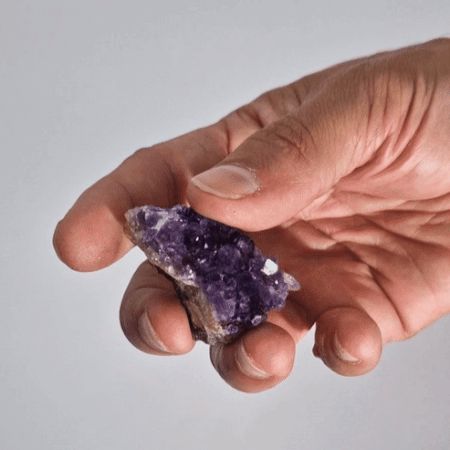 Cristal de amatista morado en mano, con facetas brillantes y textura rugosa, ideal para joyería o decoración.
