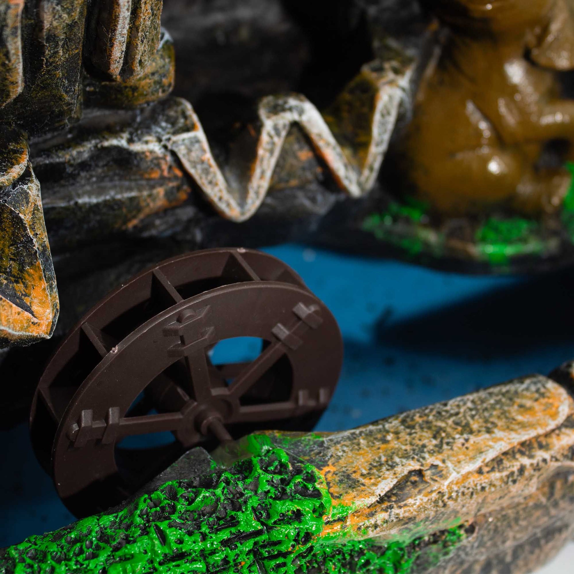 Rueda de agua marrón con detalles en piedras grises y verdes, ideal para decoración de fuentes o jardines.