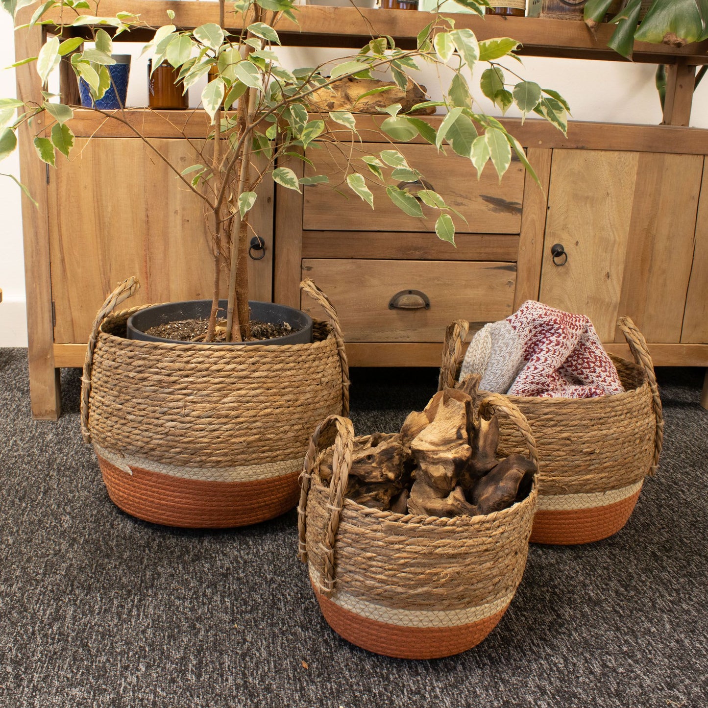 Set de 3 cestas redondas de paja y pasto marino con base naranja y asas, estilo rústico frente a un mueble de madera.