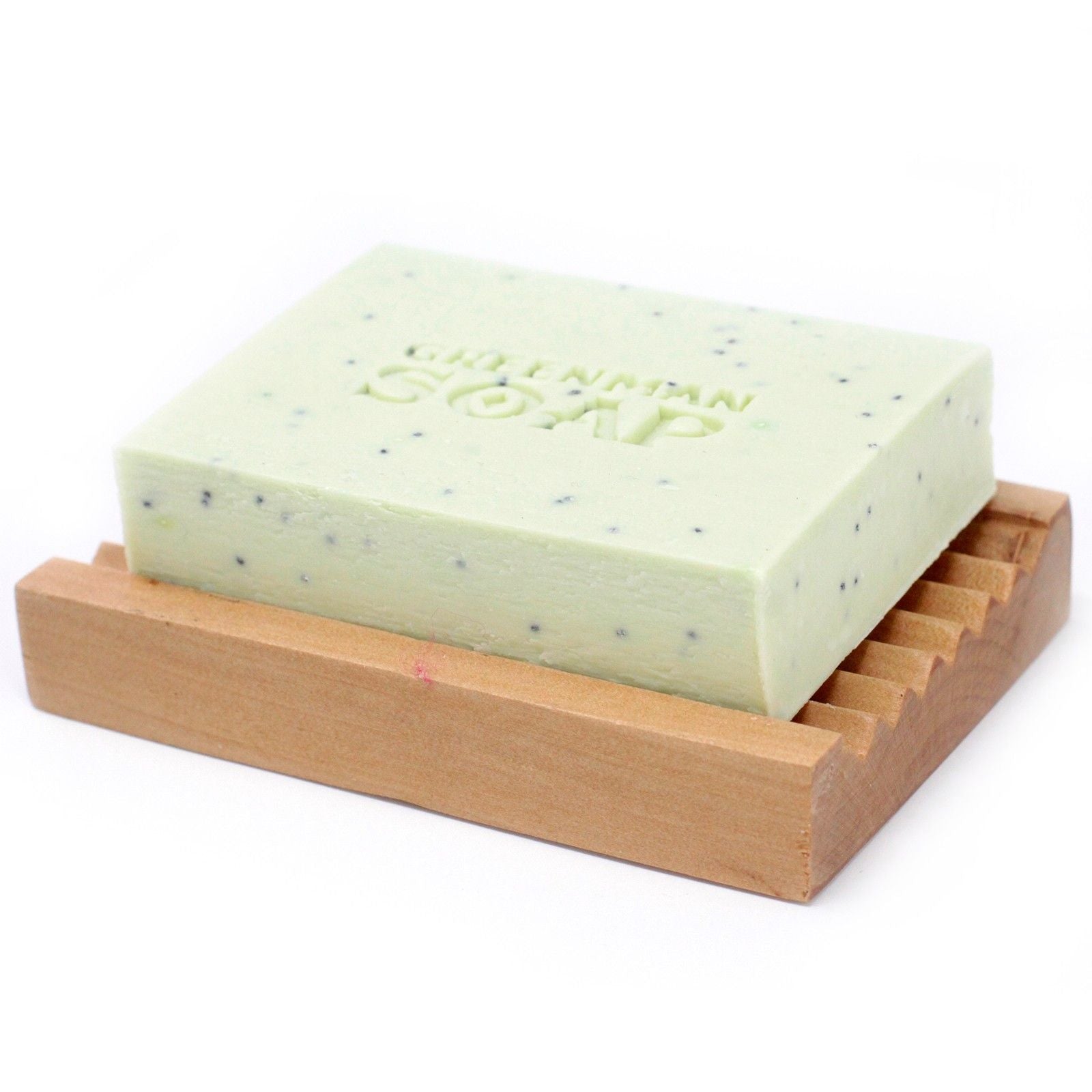 Jabón verde con puntos oscuros y grabado "GREENMAN SOAP" sobre una jabonera de madera acanalada. Fondo blanco.