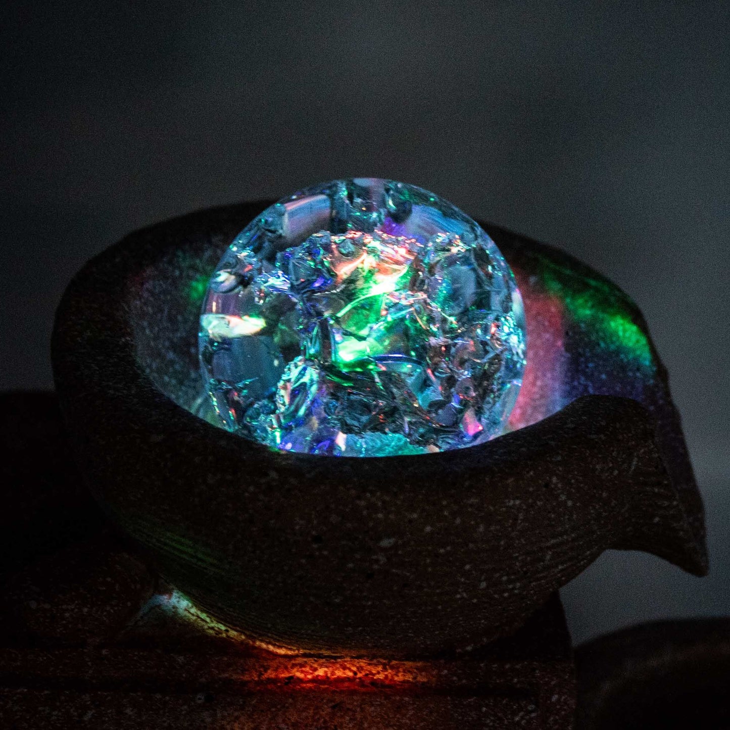 Esfera decorativa de cristal azul y verde sobre base de cerámica marrón, con luces LED multicolores.