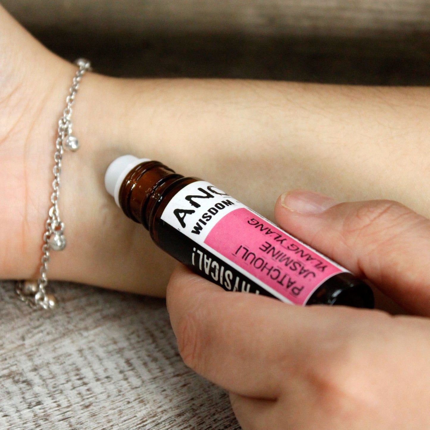 Aceite esencial de pachulí, frasco ámbar, aplicador roll-on, pulsera de plata, fondo de madera clara.