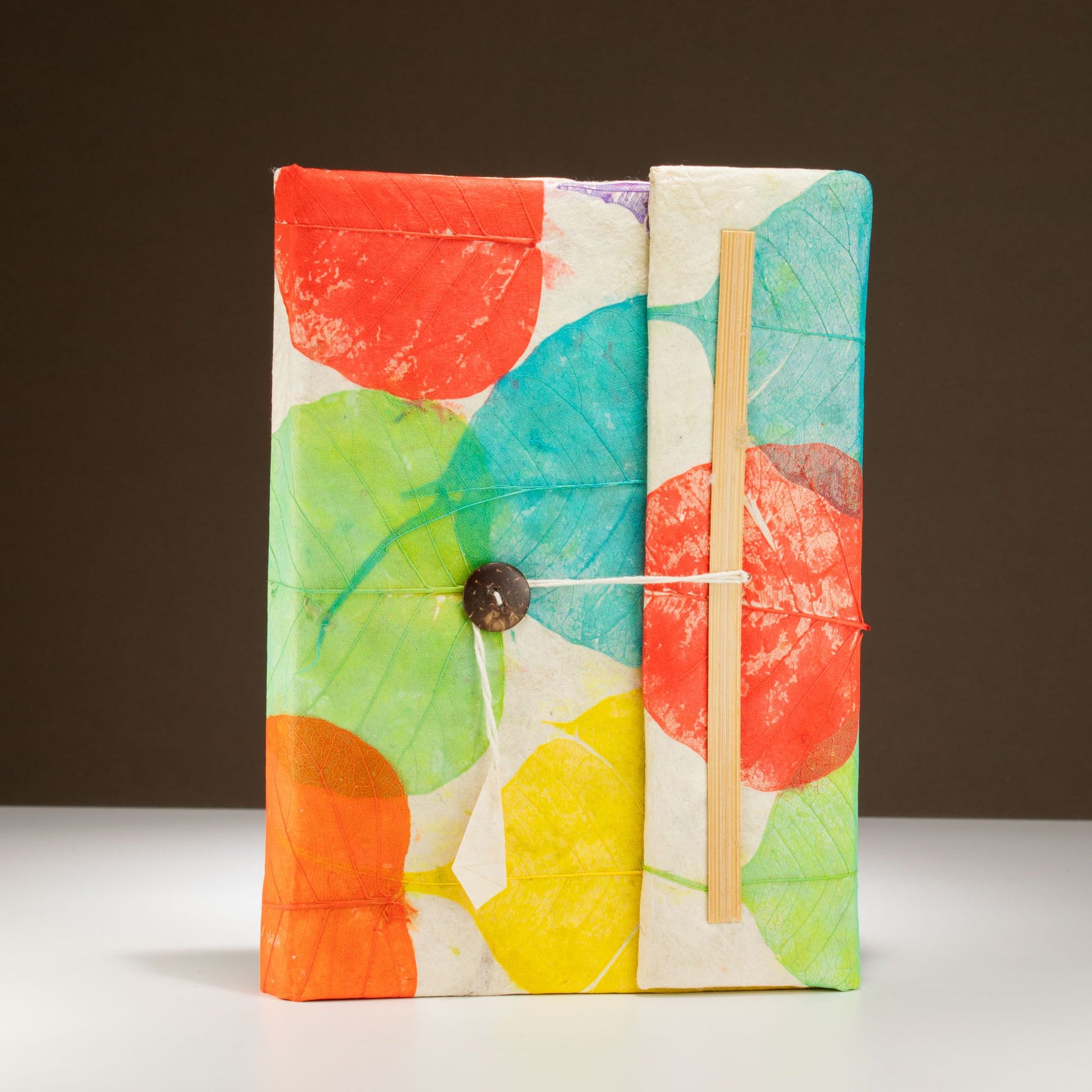 Cuadernos de papel reciclado con diseño colorido en rojo, verde y azul, atados con cuerda y botón.