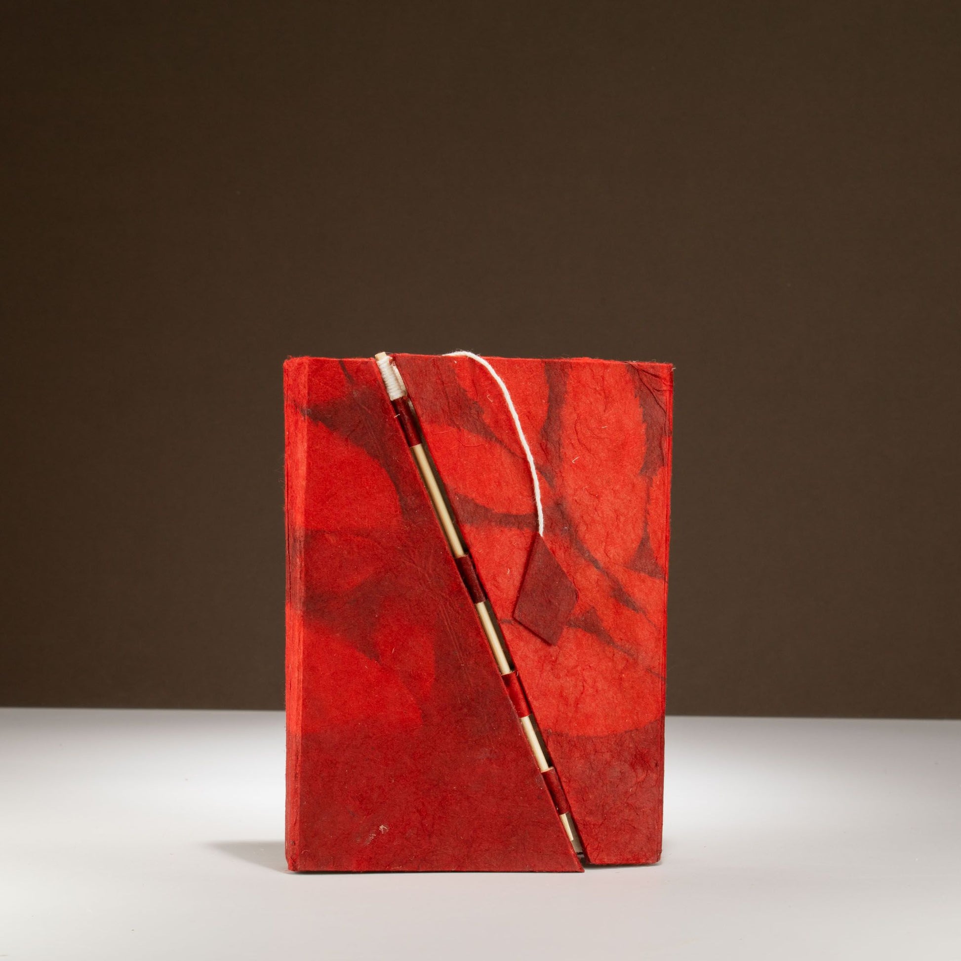 Cuaderno rojo de papel reciclado con pluma dorada, estilo artesanal y diseño de mármol. Ideal para escritura creativa.