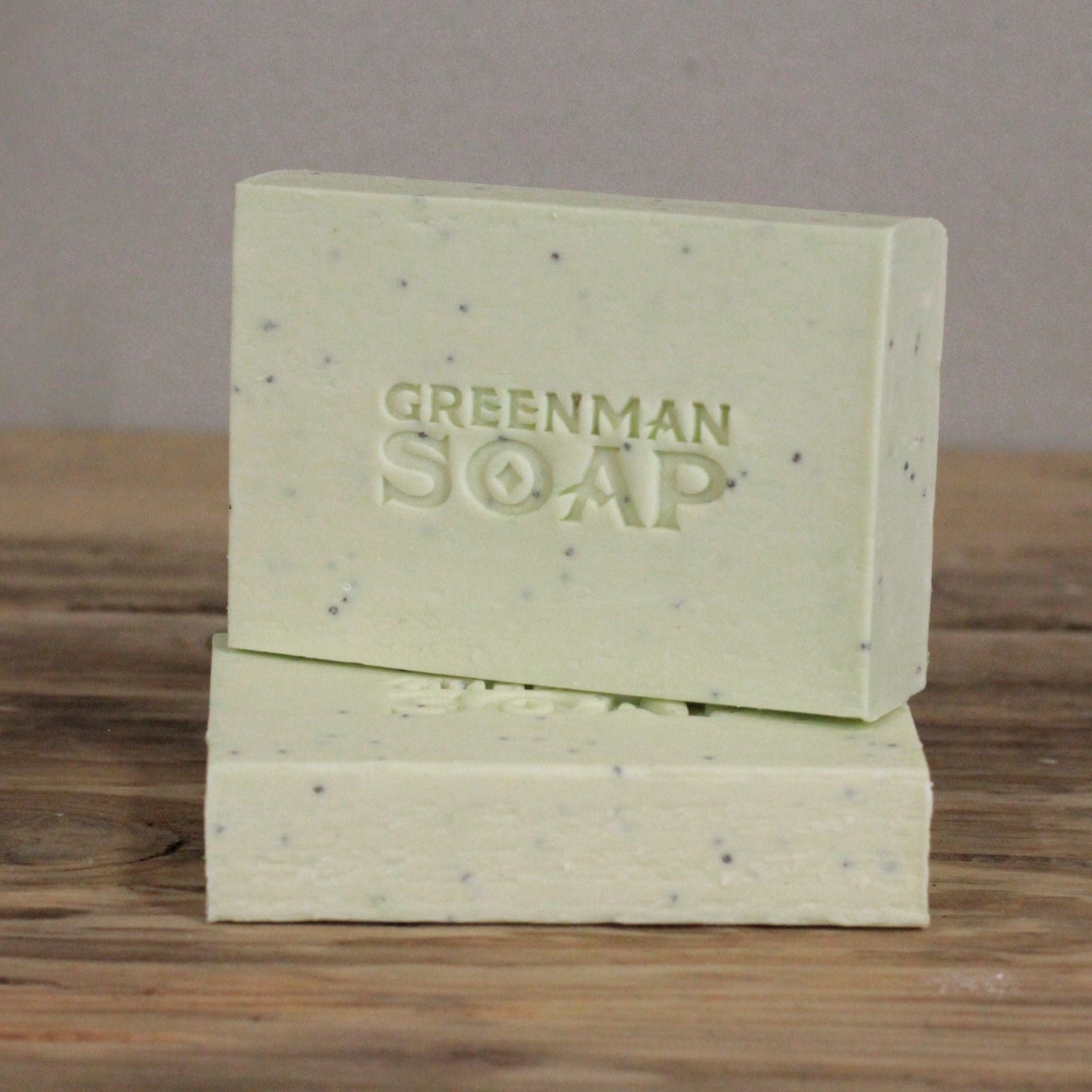 Dos barras de jabón artesanal verde claro con motas oscuras y el sello "Greenman Soap" sobre superficie de madera.