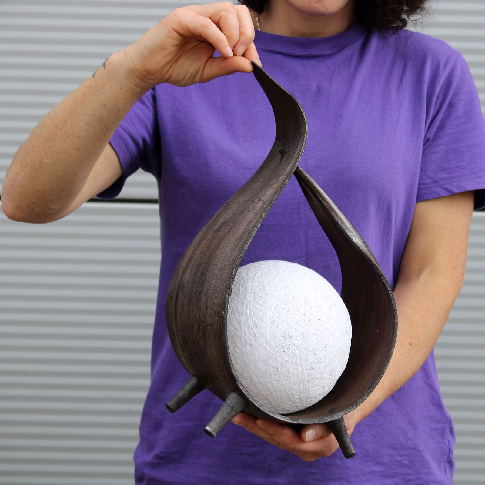 Jarrón moderno de madera oscura con diseño curvado, sosteniendo una esfera blanca decorativa.