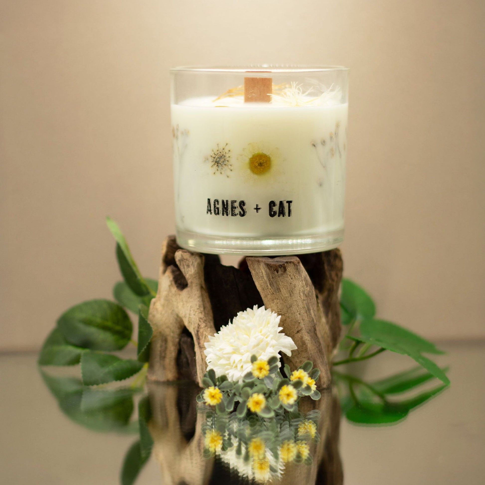 Vela blanca decorativa con flores secas, envase de vidrio, marca Agnes + Cat, sobre base de madera natural.