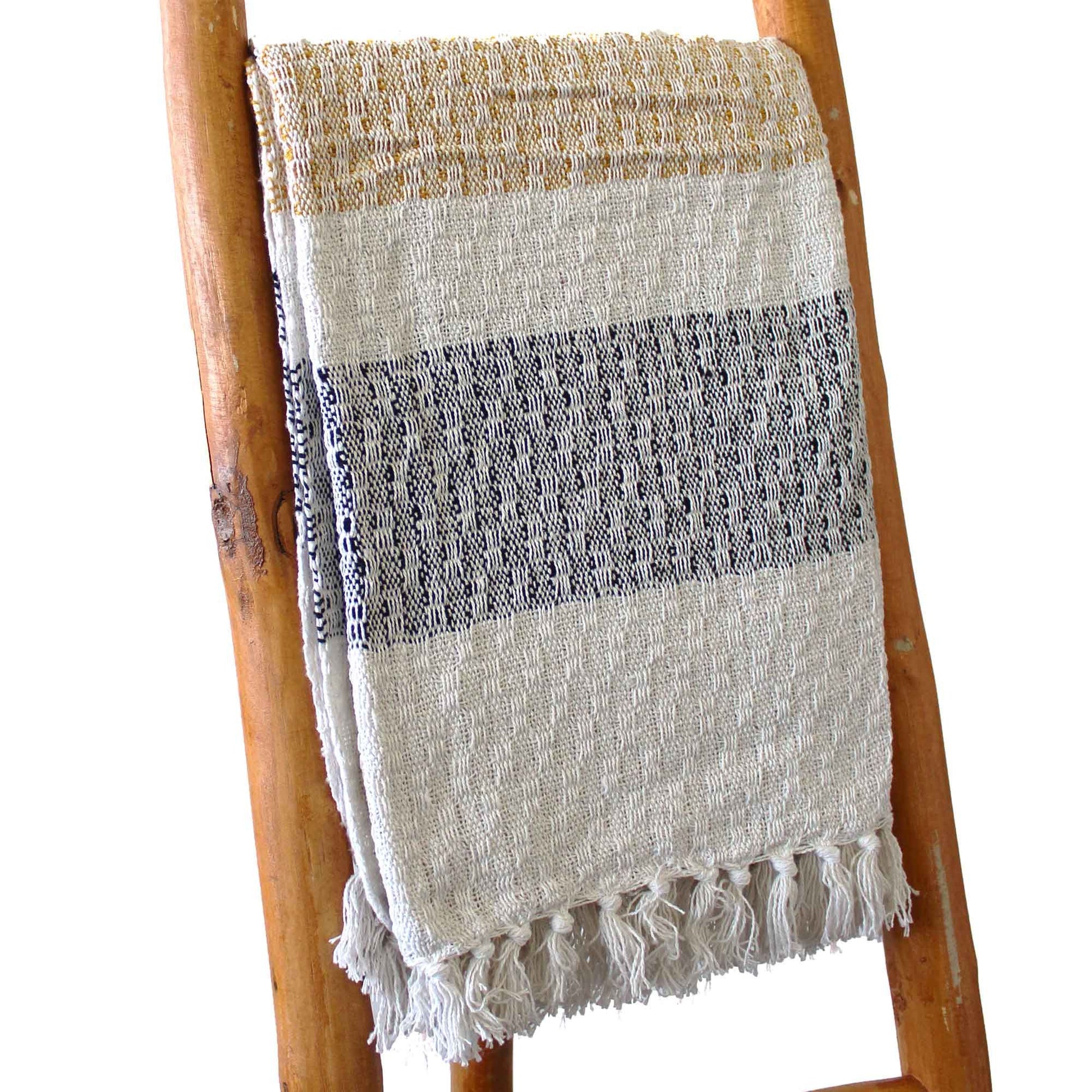 Toalla de algodón beige con franjas negras y doradas, estilo artesanal, decorativa con flecos.