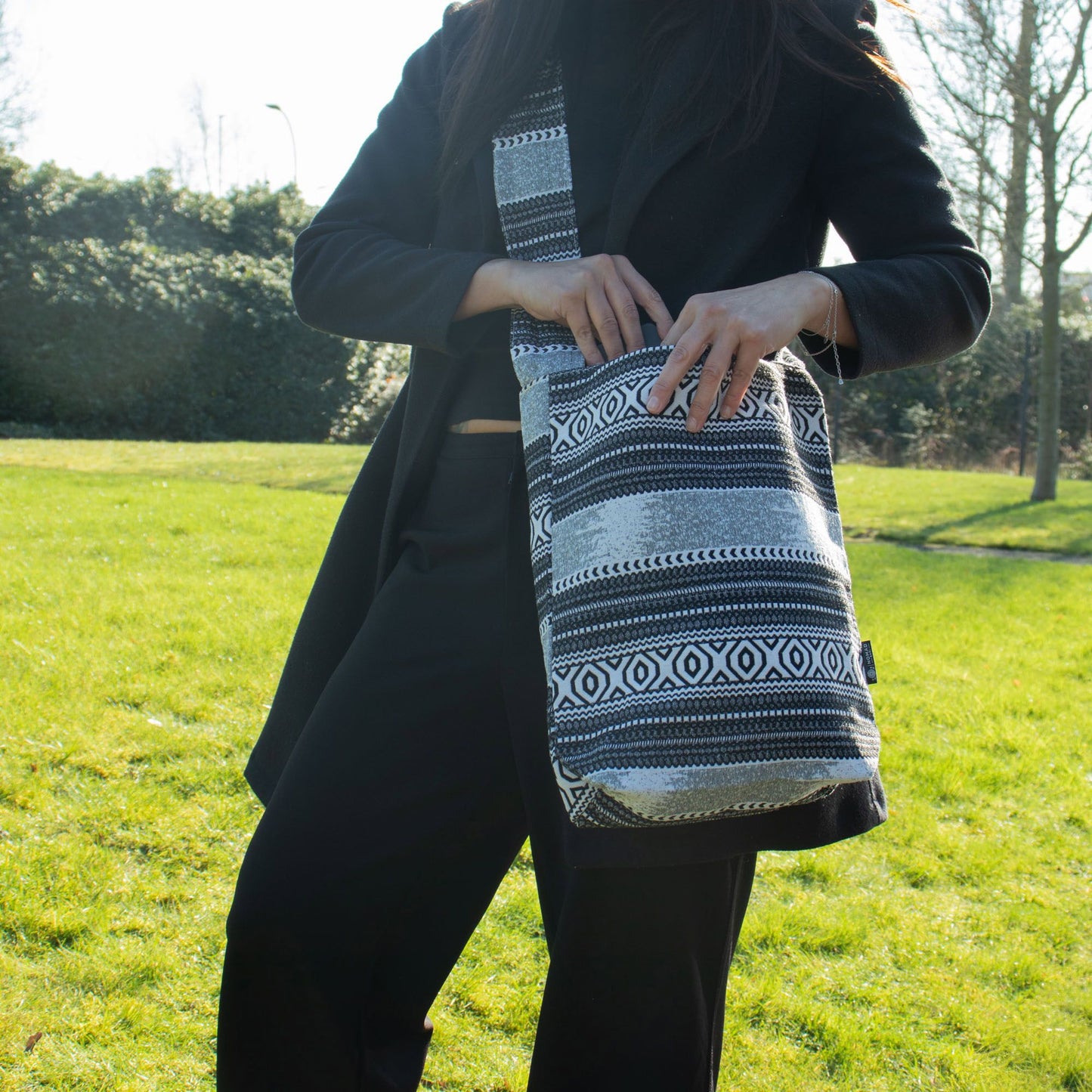 Bolso bandolera de tela gris y negro con diseño étnico, ideal para un look casual y moderno.