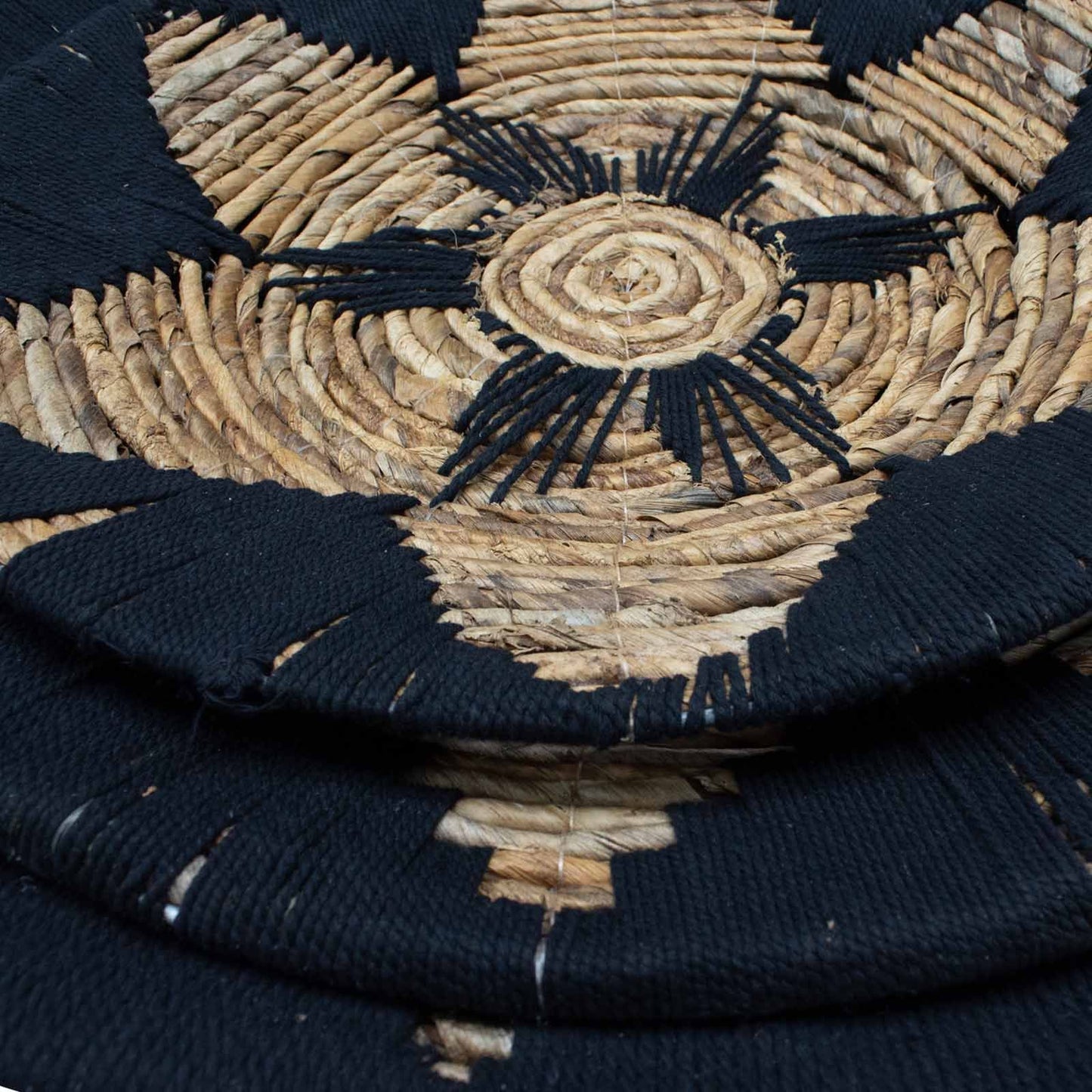 Tapete artesanal negro y natural, tejido de fibra de yute, diseño circular con motivos geométricos.