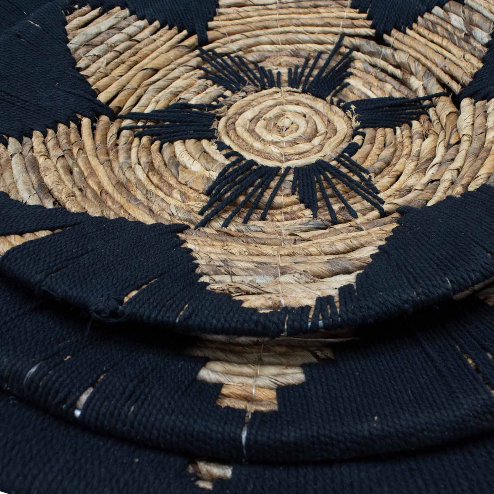 Tapete artesanal negro y natural, tejido de fibra de yute, diseño circular con motivos geométricos.