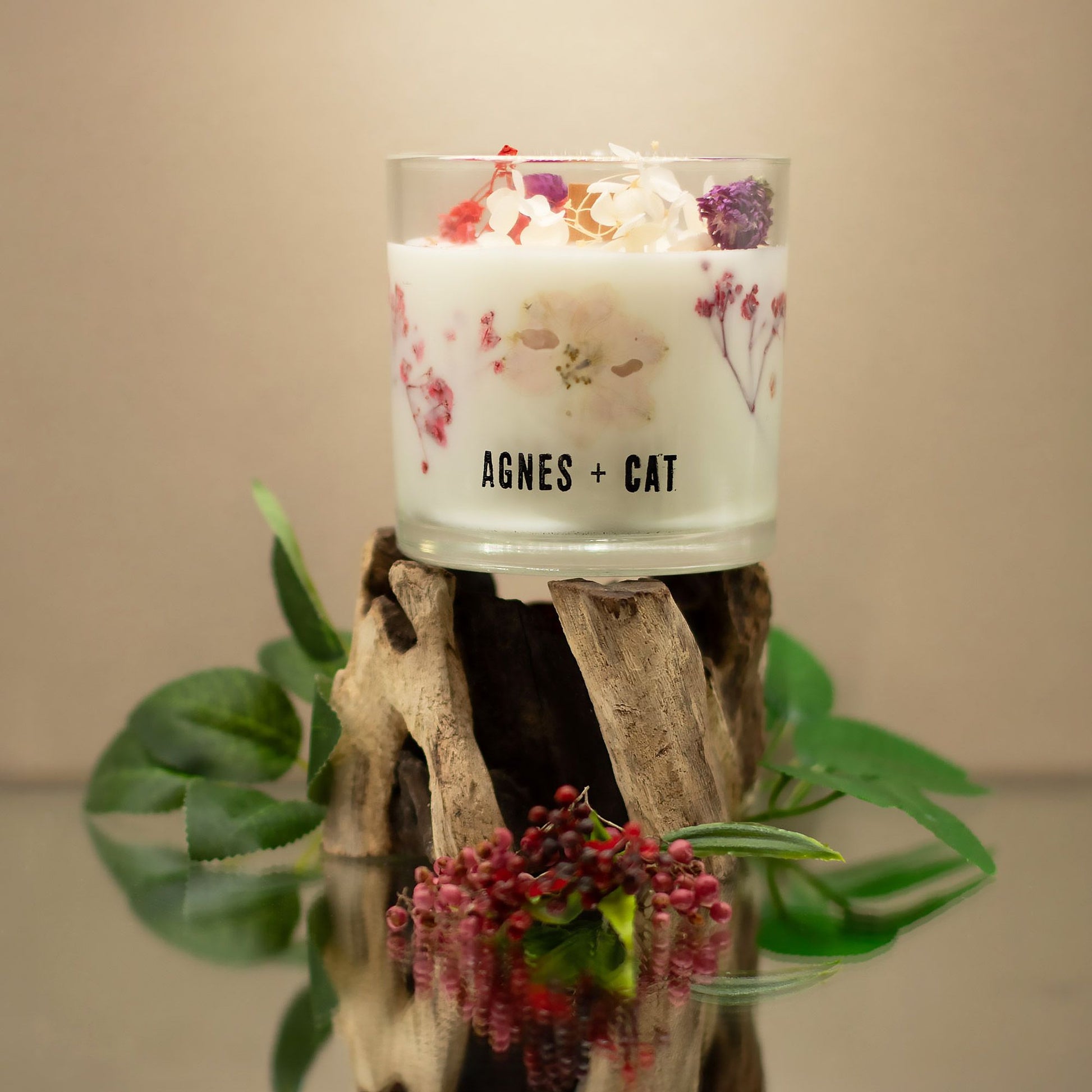 Vela aromática blanca con flores secas en vidrio, estilo elegante, marca Agnes + Cat, sobre soporte natural.