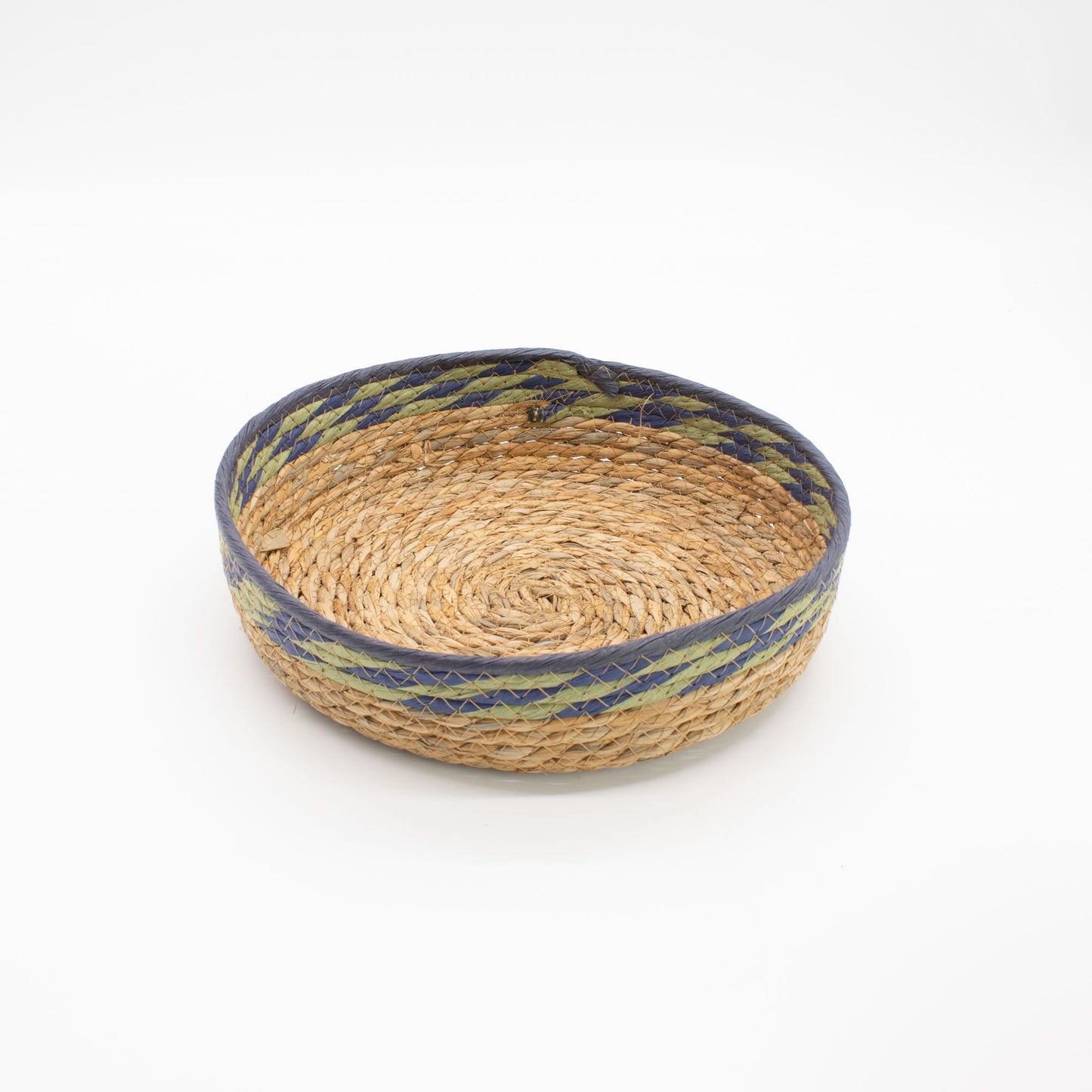 Cesta redonda artesanal de fibra natural con borde decorado en tonos verde y azul sobre fondo blanco.