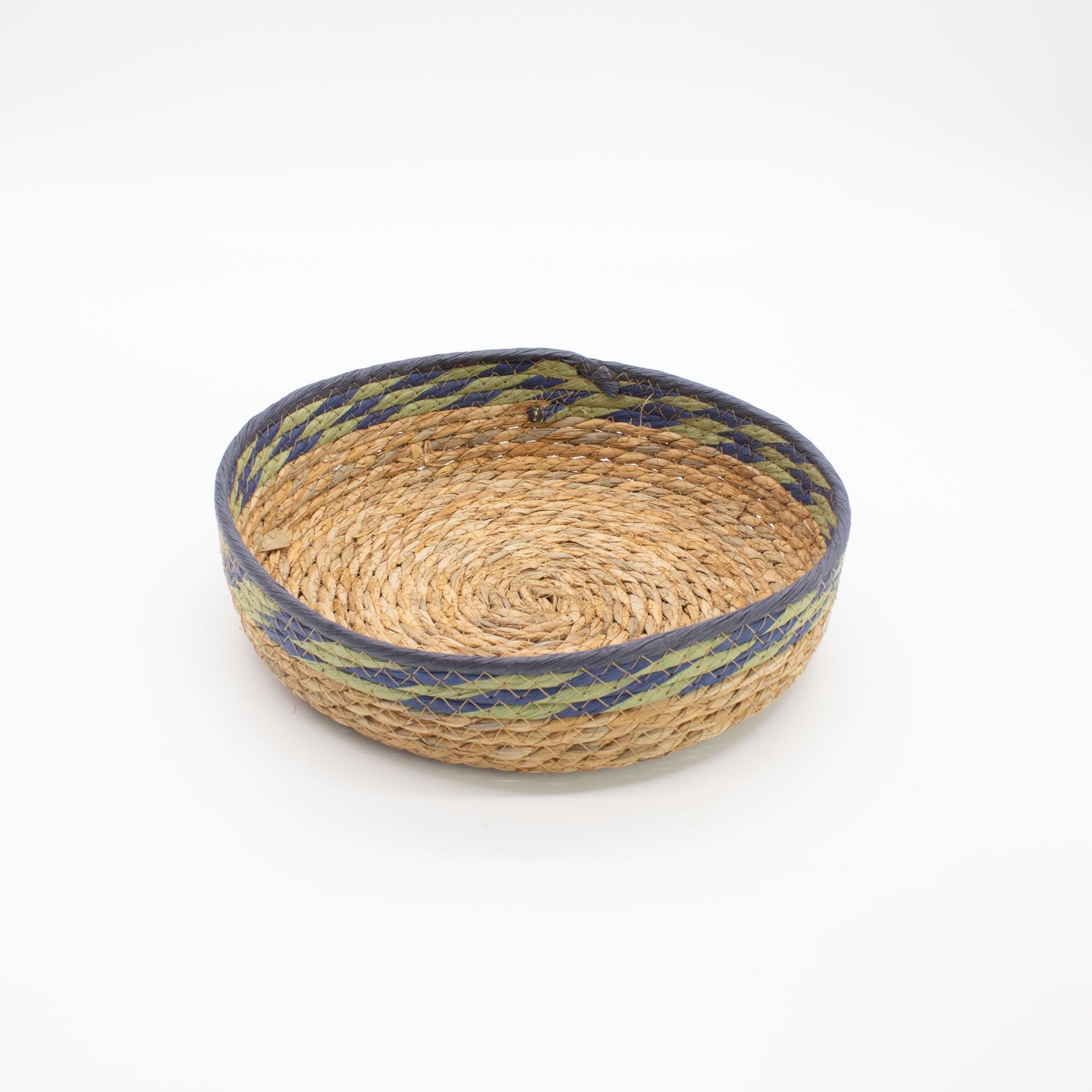Cesta redonda artesanal de fibra natural con borde decorado en tonos verde y azul sobre fondo blanco.
