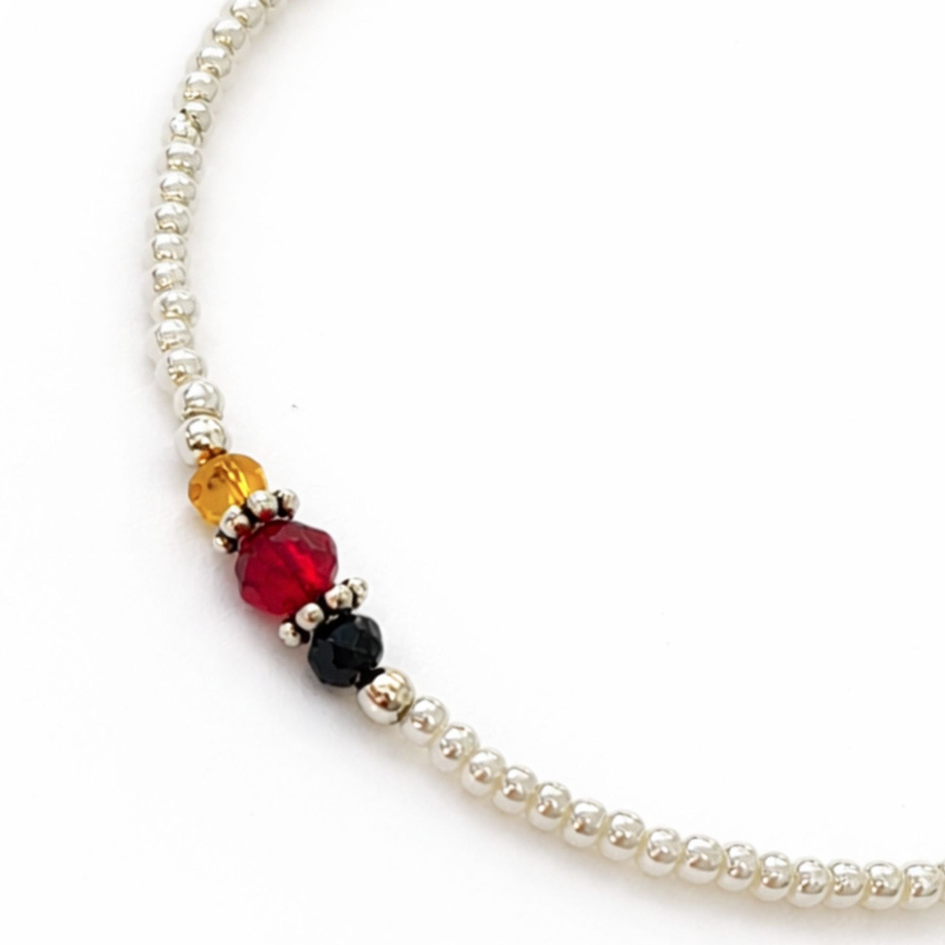 Collar de perlas plateadas con cuentas de cristal rojo, negro y ámbar, estilo elegante y moderno.