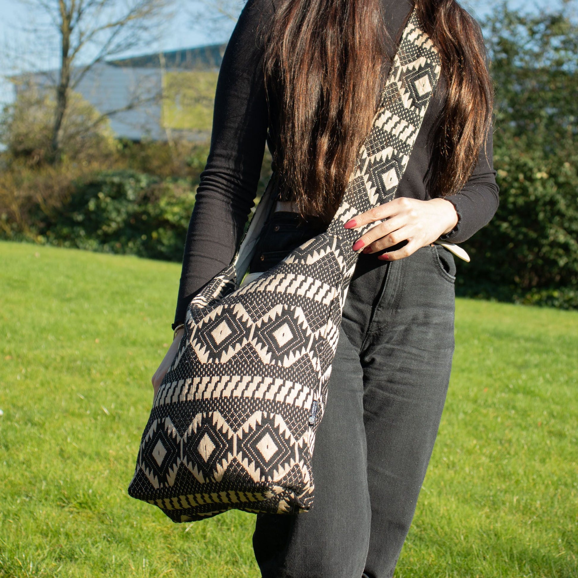 Bolso hippie bohemio en tonos negro y beige, con diseño geométrico y correa ajustable, ideal para un estilo casual.