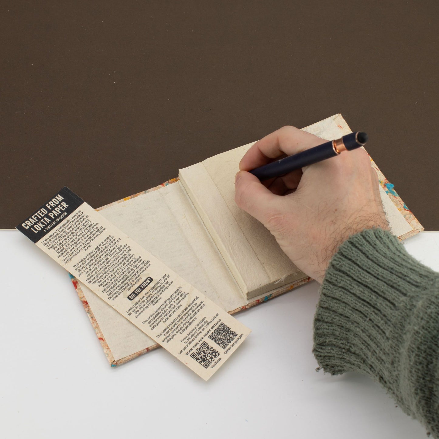 Cuaderno artesanal de papel ecológico, cubiertas multicolores y etiqueta de información, mano escribiendo con pluma.