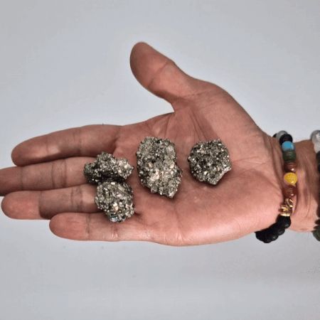 Piedras de pirita brillante, color gris metálico, en la mano, ideal para joyería y decoraciones.