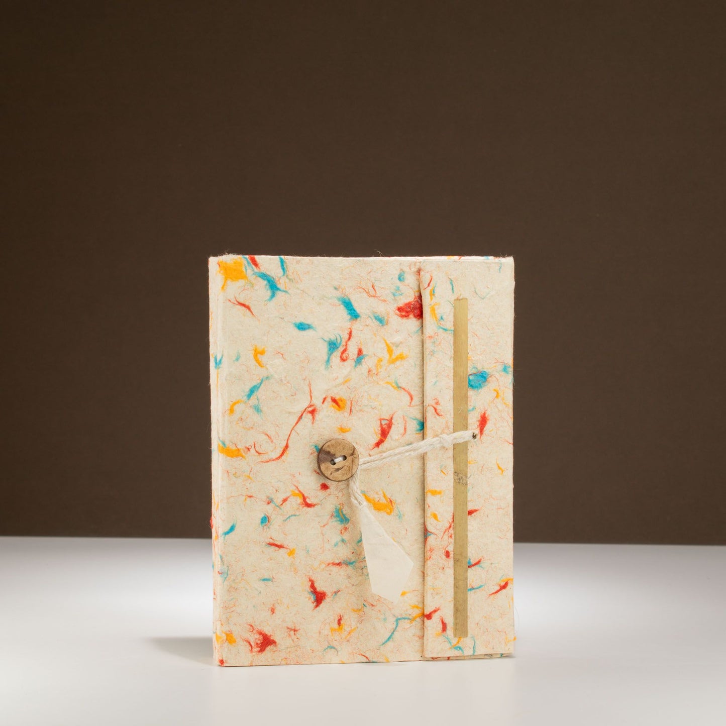 Cuaderno artesanal en tonos beige y colores vibrantes, con cierre de cuerda y detalle de madera.