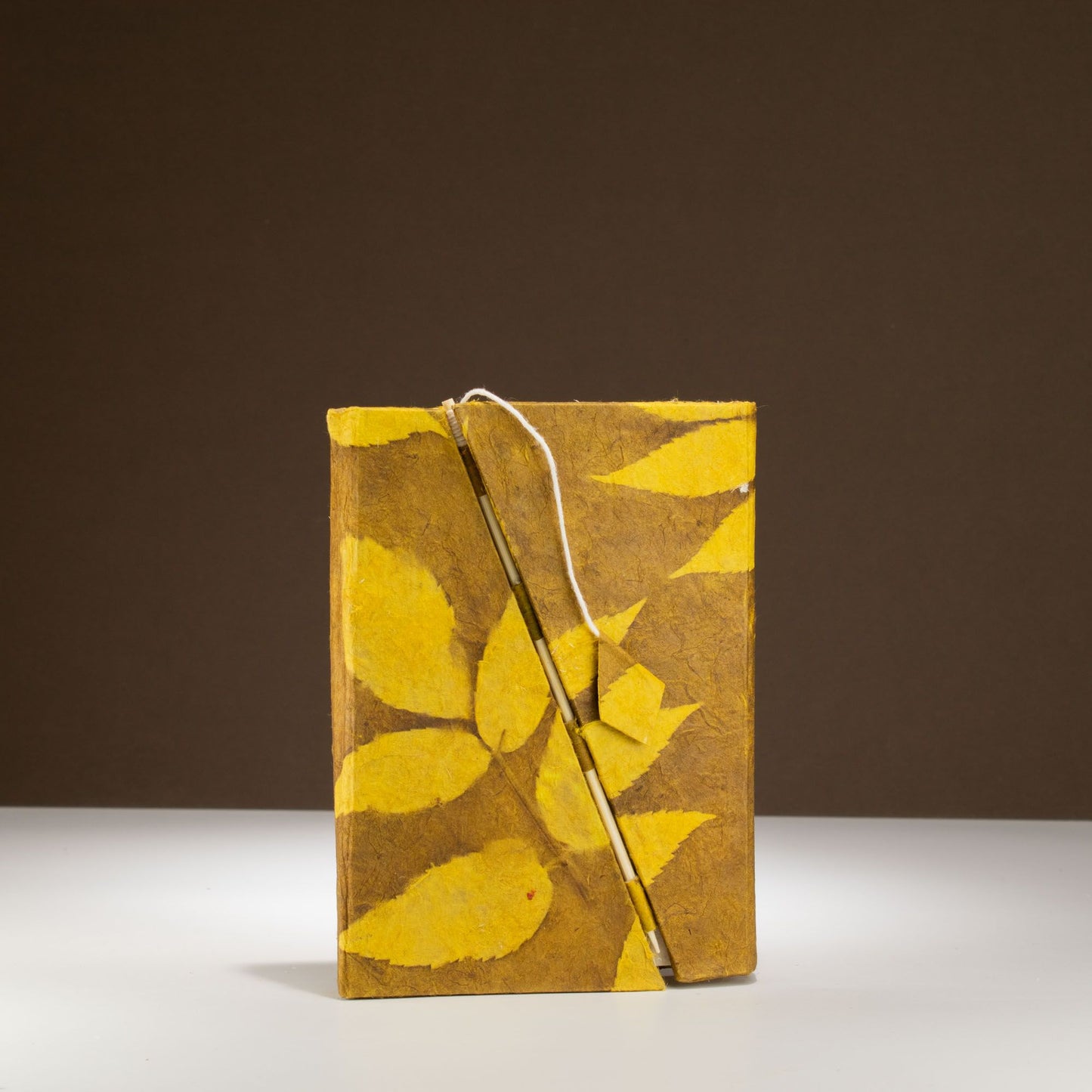 Cuaderno artesanal en papel reciclado, color marrón con hojas amarillas decorativas y cierre de cuerda.