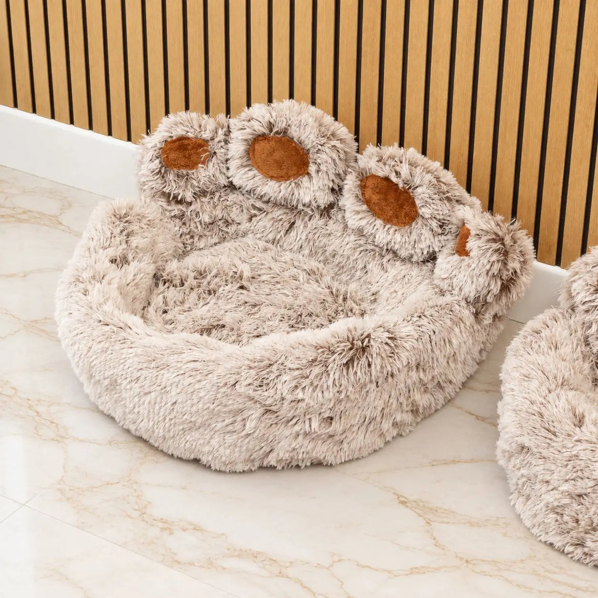 Cama con forma de huella y almohadillas marrones junto a otro modelo parcialmente visible
