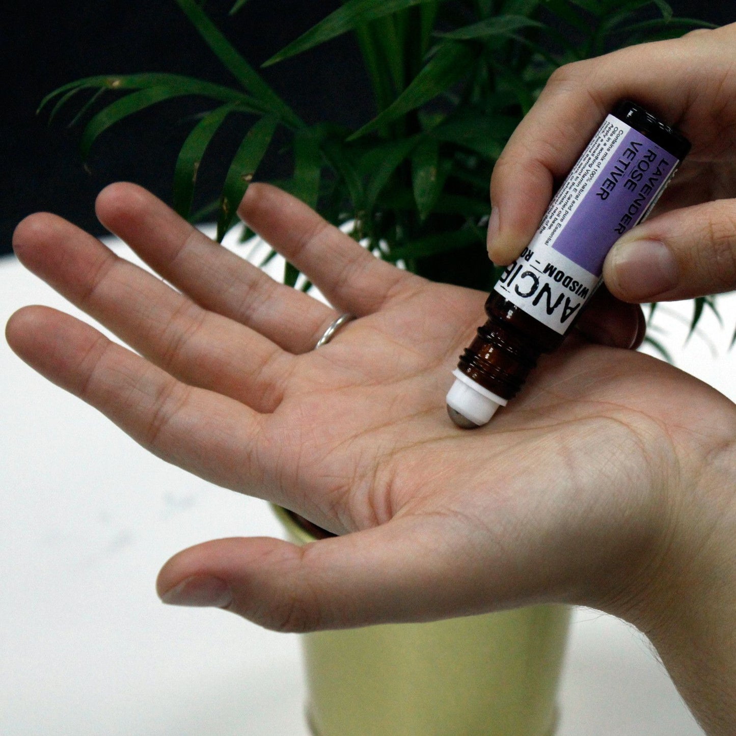 Aceite esencial de 10 ml en frasco marrón, aplicador en roll-on, manos sobre una palma, fondo verde.