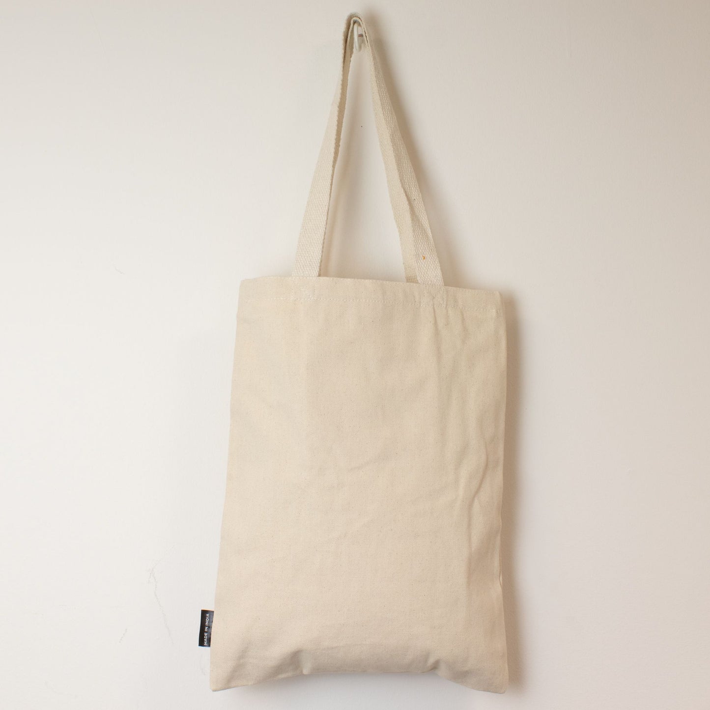 Bolsa de tela beige, estilo tote, fabricada en algodón, con asas largas y diseño minimalista.