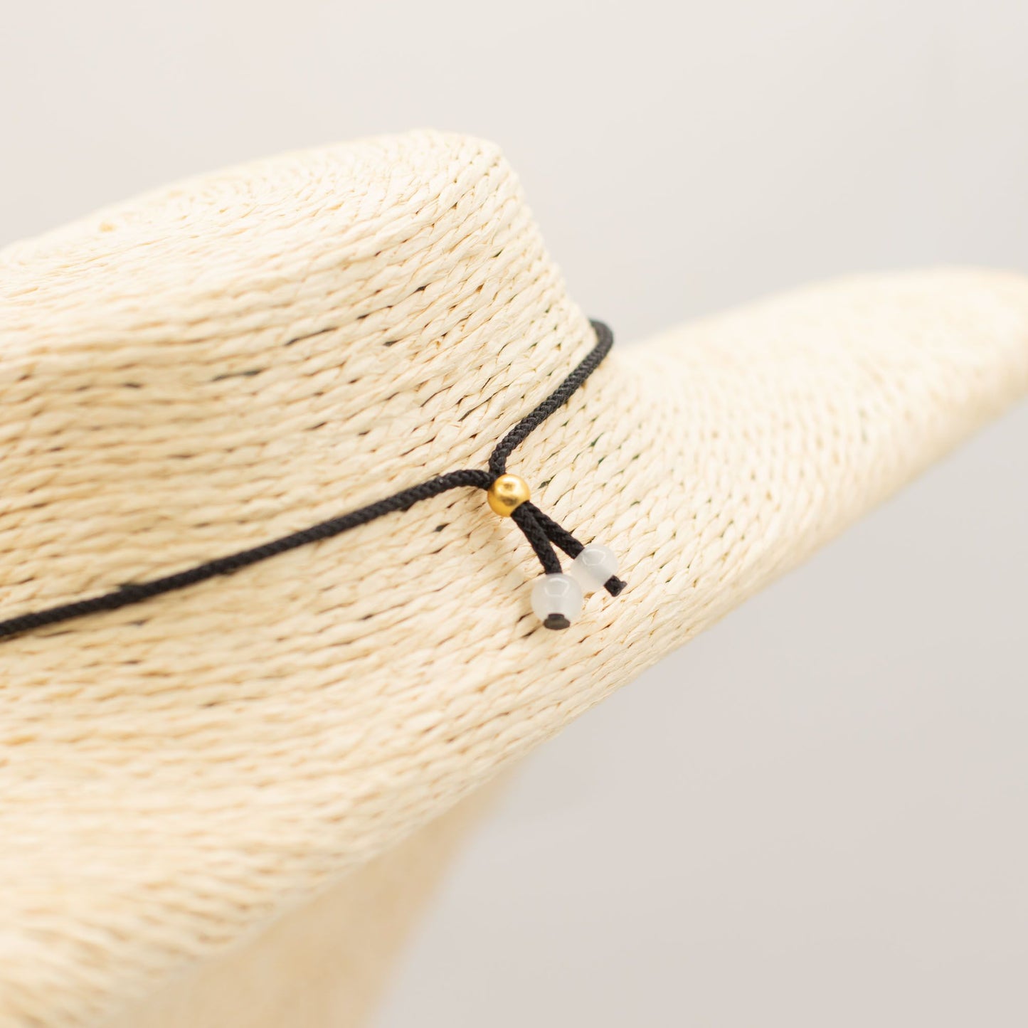 Sombrero de paja beige con cinta negra decorada con cuentas doradas y blancas, estilo bohemio y elegante.