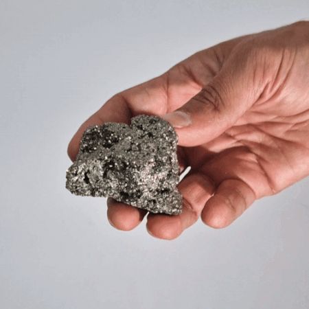 Piedra mineral bruta gris metálico en mano, textura brillante y rugosa, ideal para decoración y coleccionismo.
