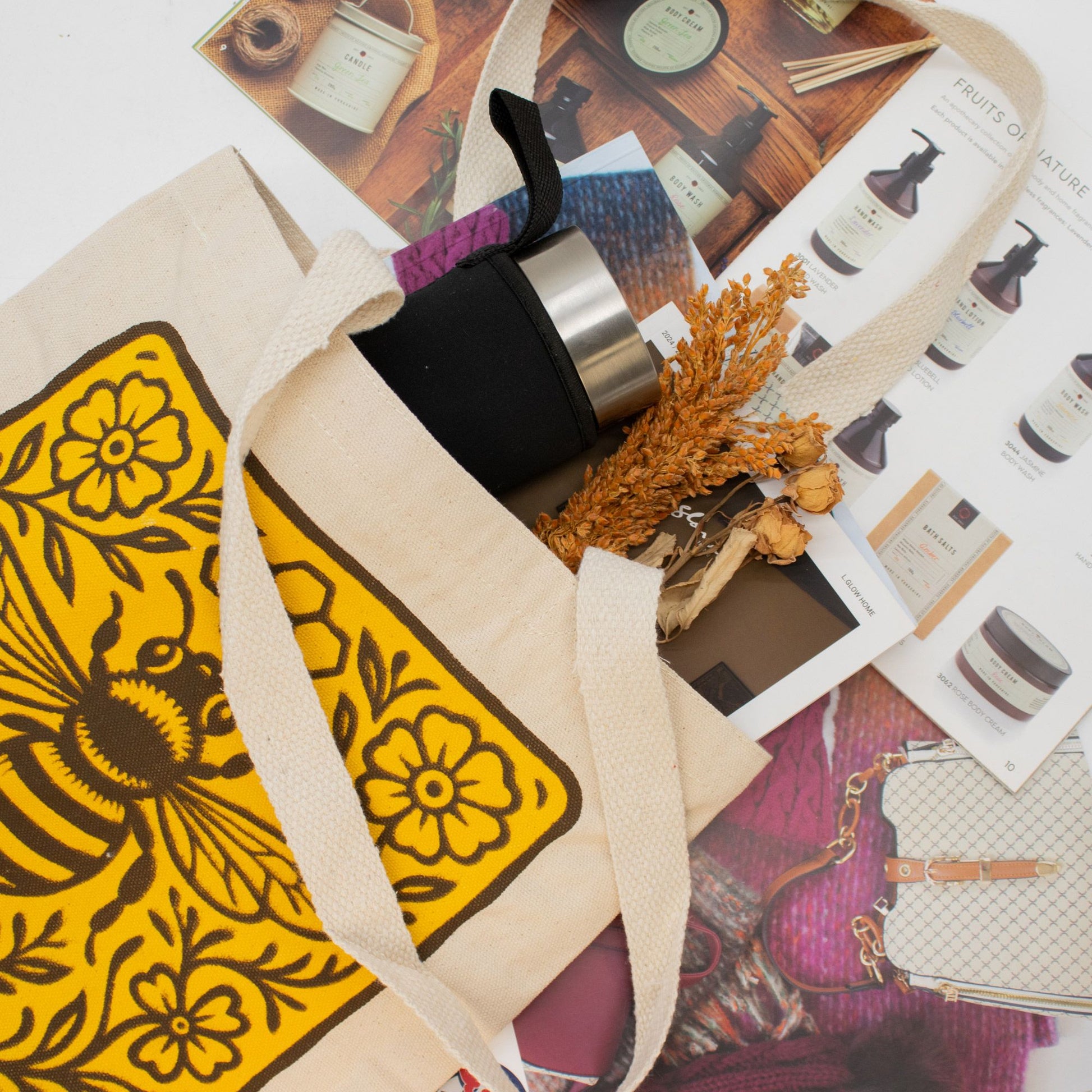 Bolso de tela beige con diseño de abeja amarilla, botella negra y detalles naturales en tonos tierra.