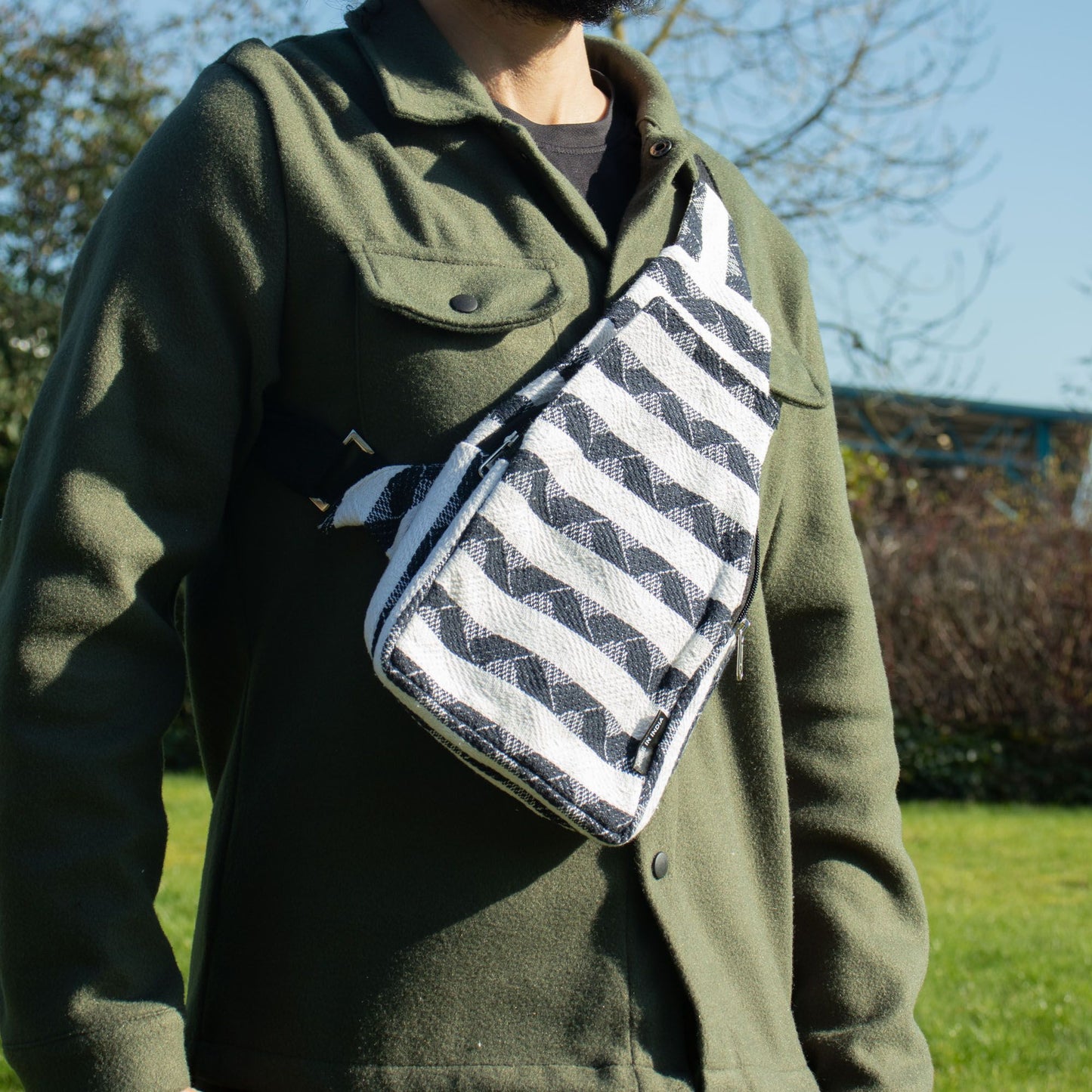 Bandolera negra y blanca de tejido con rayas, estilo moderno, sobre fondo verde natural.