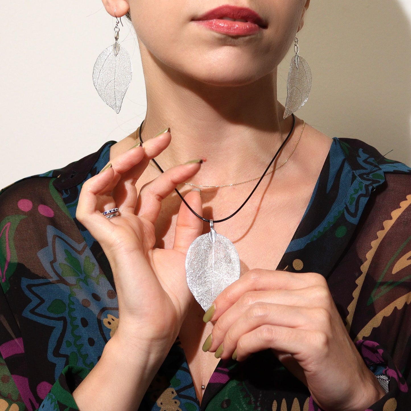 Collar y aretes de hoja en plata, detalles metálicos, diseño elegante, combinados con blusa colorida y estampado.