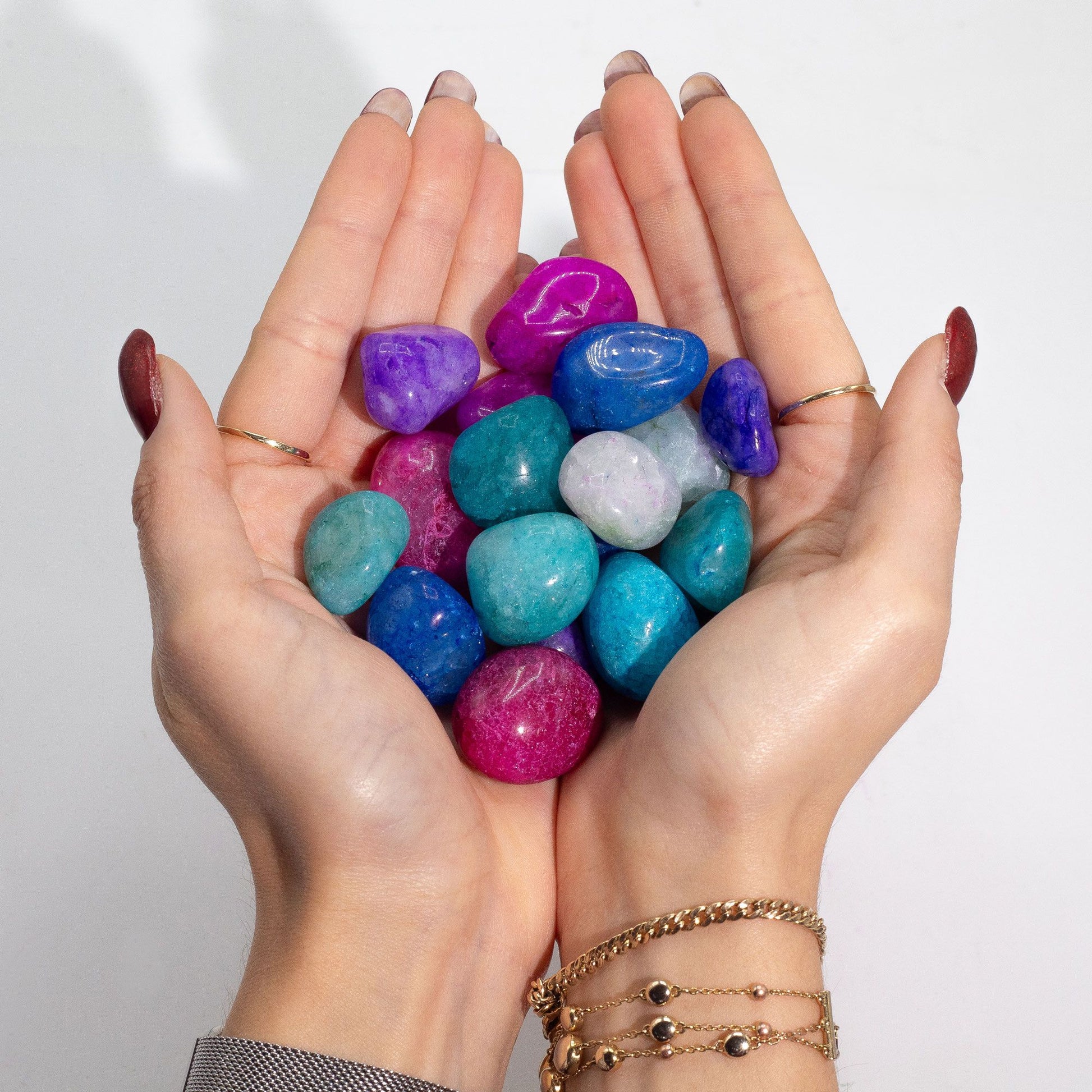Piedras de colores vibrantes en tonos púrpura, verde y azul, sostenidas en manos delicadas.